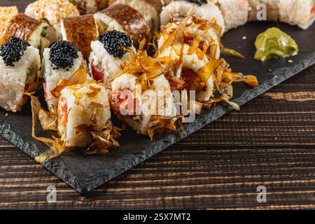 Una selezione di sushi roll disposti su un piatto di ardesia nero presenta vari ingredienti. I panini presentano pesce, riso e condimenti come uova di pesce e. Foto Stock