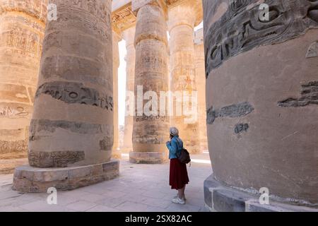 Donna viaggiatore esplora le rovine dell'antico tempio di Karnak nella città di Luxor in Egitto. Grande fila di colonne con geroglifo scolpito Foto Stock
