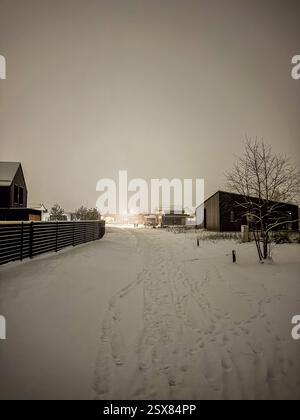 La strada del villaggio coperta di neve si illumina sotto le calde luci notturne d'inverno. Foto di alta qualità Foto Stock