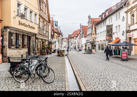 Case a graticcio, tra cui il ristorante "Fränkische Bierstube", costeggiano la strada acciottolata Hauptstraße nel centro storico di Forchheim. I pedoni passano davanti ai negozi, le biciclette sono parcheggiate sul ciglio della strada e un cartello pubblicizza una vendita di abbigliamento al 70 percento. Forchheim, Bavaria, Germania. Foto Stock