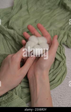 La donna tiene in mano e tocca il ramo della pianta di infiorescenza di cotone su uno sfondo di tessuto verde. Primavera Foto Stock