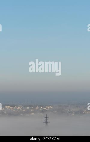 Una torre di trasmissione che emerge da una fitta nebbia sotto un cielo blu. Foto Stock