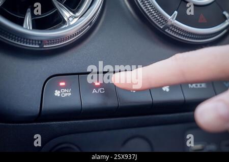 Sistema di comando della climatizzazione interna dell'auto dotato di pulsanti di comando dell'aria condizionata per il massimo comfort. Vista ravvicinata di un dito che aziona i comandi per Foto Stock