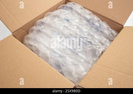Scatola di cartone aperta, piena di pellicola a bolle d'aria, messa a fuoco morbida in primo piano sul bianco Foto Stock