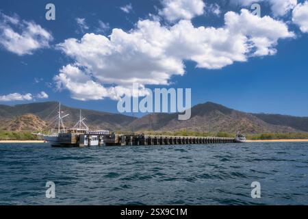 Un panorama costiero mozzafiato caratterizzato da un'affascinante piccola barca turistica ancorata saldamente in un molo pittoresco, perfettamente adagiata su maestose montagne e Foto Stock