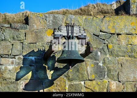 Una vecchia campana è appesa a una robusta struttura in legno fissata ad una parete di pietra intemprata. La luce del sole proietta ombre, evidenziando i dettagli intricati del Be Foto Stock