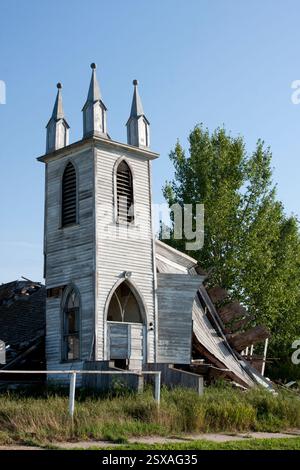 La chiesa presenta un tetto rotto e un grande albero di fronte. La chiesa è vecchia e abbandonata Foto Stock