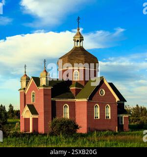 Chiesa in mattoni rossi con tetto verde. Il tetto è coperto di muschio. La chiesa è circondata da un campo Foto Stock