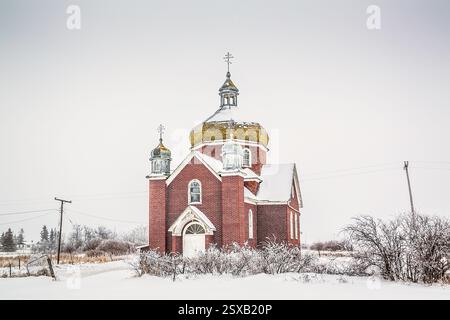 Chiesa in mattoni rossi con un campanile e una croce in cima. Il tetto è coperto di neve Foto Stock