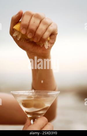 Tagliato a mano, spremendo il succo di limone in un bicchiere di cocktail giallo trasparente. Foto Stock