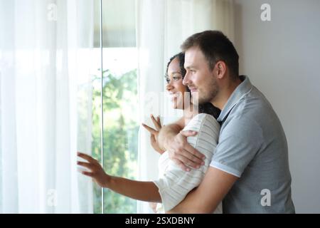 Coppia interrazziale che guarda dalla finestra di casa o della camera d'albergo Foto Stock