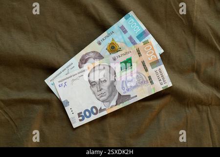 Le banconote ucraine in tagli da 500 e 1.000 si trovano su tessuto di colore militare, affari e finanza, moneta Foto Stock