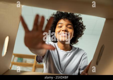 Vista inferiore interno della scatola di cartone. Ragazza africana che disimballa la consegna guardando nella scatola. Donna che apre la scatola di cartone. Donna che riceve un pacco che guarda gli articoli consegnati. Feedback positivo del cliente soddisfatto Foto Stock
