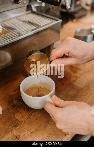Il barista versa un espresso appena estratto in una tazza di caffè bianco Foto Stock