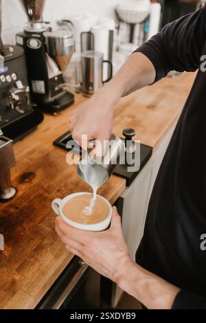 Il barista versa il latte montato nella tazza da caffè creando una latte art Foto Stock