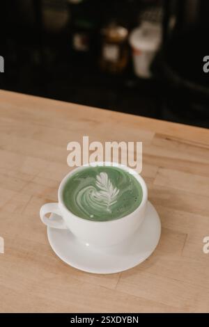 Latte Matcha con latte art in foglia in tazza bianca su bancone in legno. Foto Stock