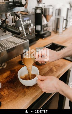 Il barista versa un espresso appena estratto in una tazza di caffè bianco Foto Stock