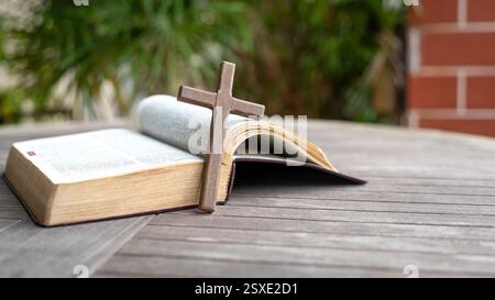 Croce crocifisso in legno accanto alla Sacra Bibbia. Sopra un tavolo di legno. Copia spazio. Foto Stock