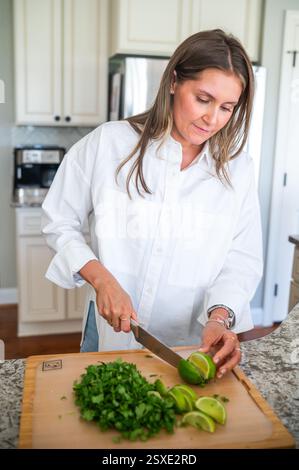 Giovane donna che taglia il lime mentre prepara la ricetta in cucina Foto Stock