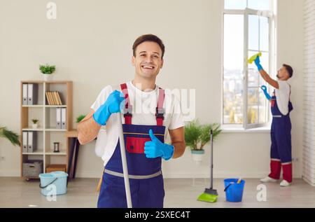 Ritratto di un inserviente maschio felice del servizio di pulizia che dava i pollici e sorrideva Foto Stock