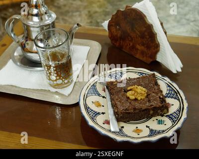 Brownie al cioccolato con noci e tè tradizionale con teiera servito su un tavolo in un caffè nella città di Essaouira, Marocco, febbraio 2025 Foto Stock