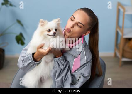 Donna che tiene in mano un pomerano mentre fa un gesto di bacio sul viso in un ambiente interno, un piccolo cane che sembra contento e tranquillo Foto Stock