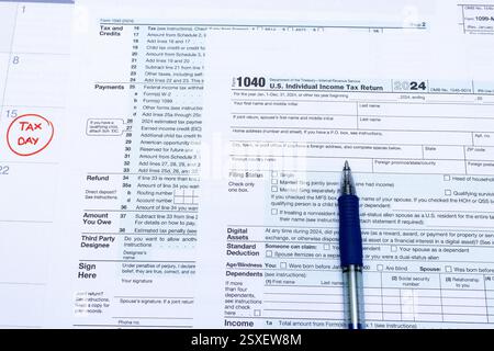 Un primo piano dei moduli fiscali statunitensi, inclusa la dichiarazione dei redditi individuali del 1040, con una penna blu appoggiata sul documento. Un calendario sullo sfondo h Foto Stock