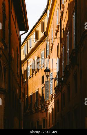 La calda luce del sole illumina una stretta strada fiancheggiata da edifici tradizionali caratterizzati da persiane bianche e balconi in ferro battuto a Verona, Italia Foto Stock