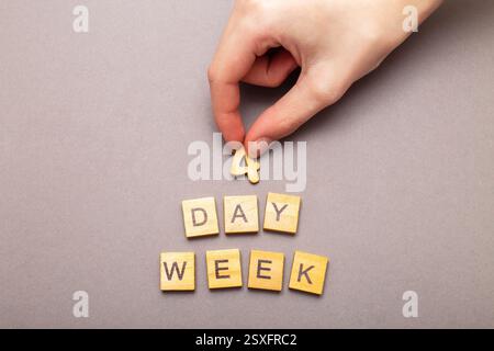Vista dall'alto dell'uomo che mette la parola quattro giorni alla settimana con cubi di legno su sfondo grigio. concetto aziendale di produttività di 4 giorni settimanali. Foto Stock