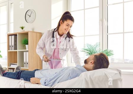 Medico donna con sorriso premuroso assiste il paziente di sesso maschile sdraiato per garantire comfort e benessere. Donna medico esemplifica professionalità compassione Foto Stock