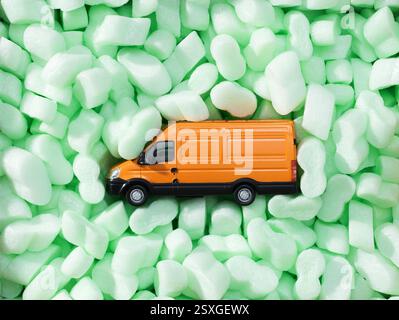Grazioso piccolo pulmino per la consegna dei giocattoli circondato da patatine di imballaggio, servizio di consegna e concetto di trasporto Foto Stock