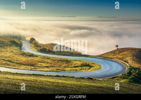 Strada con tornanti nel paesaggio toscano vicino a Volterra in una mattinata nebbiosa. Provincia di Pisa, regione Toscana, Italia Foto Stock