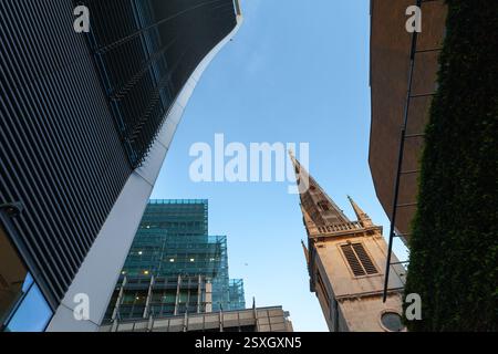 Contrasto tra grattacieli moderni e una guglia storica della chiesa, che mostra un paesaggio urbano sotto il cielo limpido. Vista sulla città di Londra Foto Stock