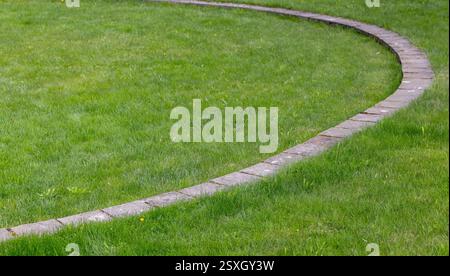 Un percorso in mattoni ben mantenuto si snoda attraverso un vivace prato verde, evocando sentimenti di ordine e bellezza naturale. Foto di sfondo astratta Foto Stock