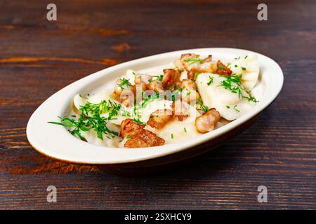 Deliziosi gnocchi fatti in casa conditi con croccante carne fritta ed erbe fresche sono serviti elegantemente su un rustico tavolo di legno. Un piatto confortante perfetto Foto Stock