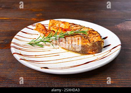 Un pezzetto di pesce grigliato splendidamente placcato guarnito con erbe fresche e tritato con glassa balsamica. Questo piatto è perfetto per un'esperienza culinaria raffinata Foto Stock