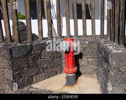 Idrante rosso installato in un recinto in pietra circondato da recinzioni in legno in un ambiente urbano all'aperto in una giornata di sole Costa Teguise Lanzarote Foto Stock