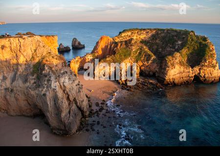 Praia de João de Arens al tramonto con formazioni rocciose e spiaggia sabbiosa, Portogallo. La luce del sole dorata bagna aspre scogliere e coste sabbiose, altissimo Foto Stock