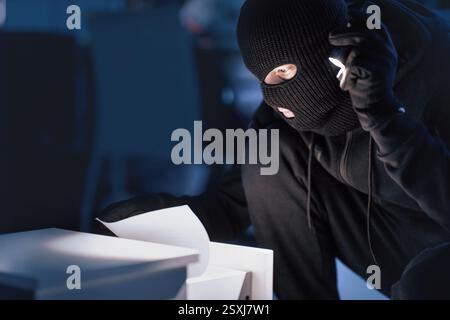 Ladro mascherato che tiene e legge documenti riservati Foto Stock
