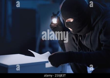 Intruso mascherato che tiene e legge documenti riservati Foto Stock