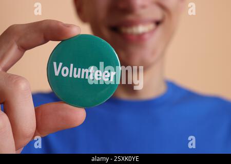 Uomo che tiene in mano il distintivo con la parola Volunteer su sfondo beige, primo piano Foto Stock