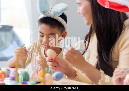 Felicità di Pasqua. Una madre e i bambini amano dipingere insieme le uova di Pasqua a un tavolo festivo, festeggiando la vacanza con divertimento e creatività. Pasqua da Foto Stock
