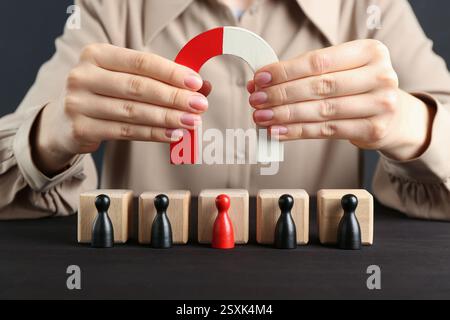 Donna con magnete che attrae pezzi da gioco al tavolo di legno, primo piano Foto Stock