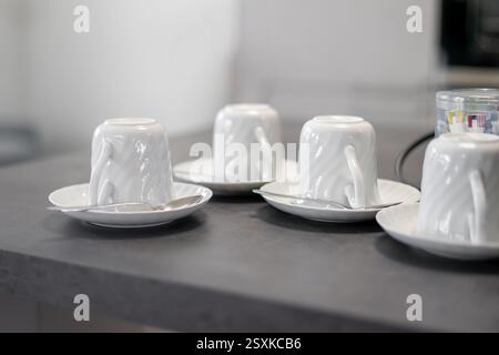 Vista dall'alto delle tazze in porcellana bianca capovolte sui piattini sul tavolo della cucina Foto Stock