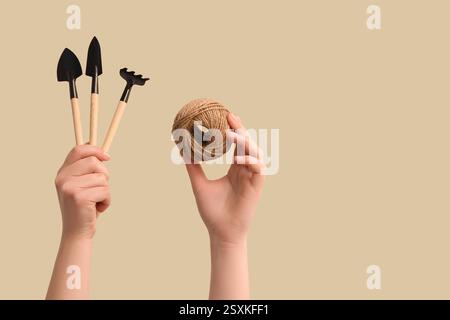 Mani femminili che reggono set di attrezzi da giardinaggio e corda su sfondo beige Foto Stock