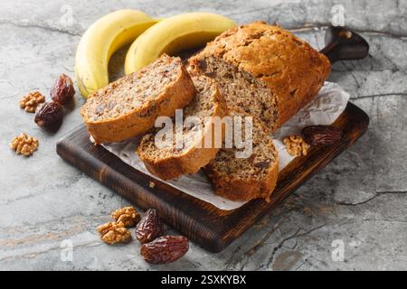 Pane di noci di banana appena sfornato circondato da ingredienti ravvicinati su una tavola di legno sul tavolo. Orizzontale Foto Stock