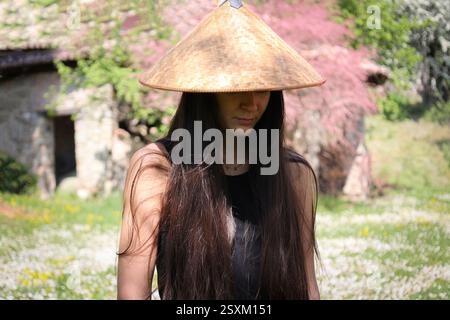 giovane donna con capelli lunghi e cappello di bambù che cammina in un campo di margherite, sfondo defocalizzato Foto Stock