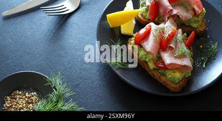 Toast all'avocado con prosciutto al forno e pomodoro su sfondo scuro. Concetto di cibo sano. Vista dall'alto. Foto Stock