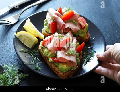 Toast all'avocado con prosciutto al forno e pomodoro su sfondo scuro. Concetto di cibo sano. Vista dall'alto. Foto Stock