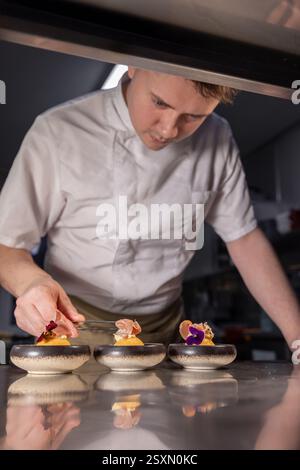 Lo chef propone piatti gourmet con fiori e prosciutto nella cucina del ristorante Foto Stock